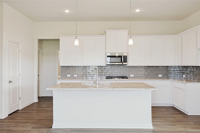 kitchen with a center island with sink, white cabinetry, pendant lighting, and light stone countertops