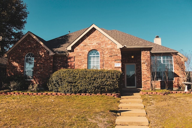 view of front of home featuring a front yard, brick siding, and a chimney