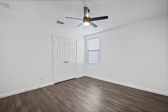 unfurnished bedroom with dark wood-type flooring, a textured ceiling, a closet, and ceiling fan