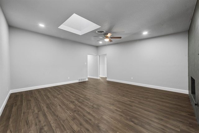 spare room featuring ceiling fan, a large fireplace, a skylight, and dark hardwood / wood-style flooring