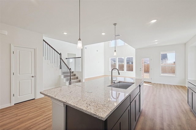 kitchen with light stone counters, sink, decorative light fixtures, and an island with sink