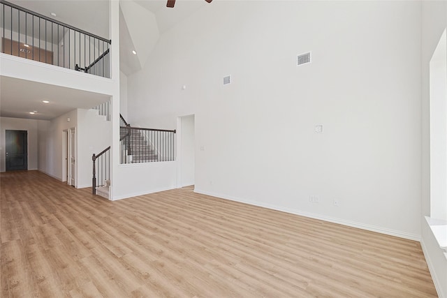 unfurnished living room featuring ceiling fan, light hardwood / wood-style floors, and a high ceiling