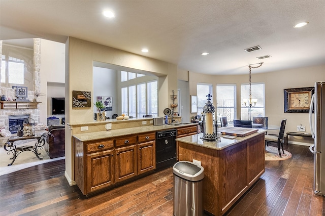 kitchen featuring visible vents, a center island, dark wood-style flooring, black dishwasher, and a stone fireplace