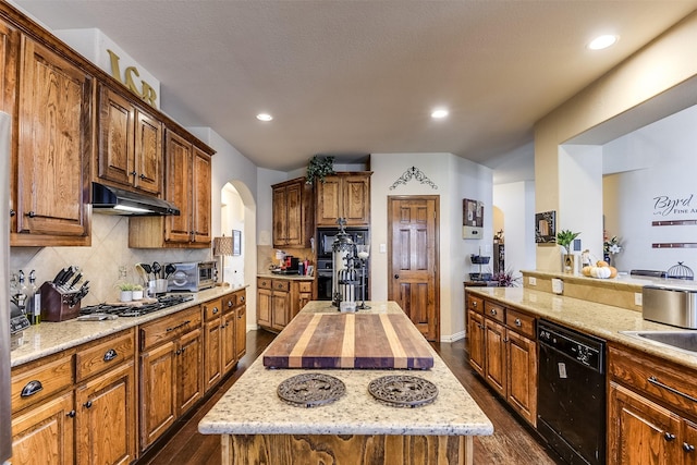 kitchen with dark wood finished floors, arched walkways, decorative backsplash, under cabinet range hood, and black appliances