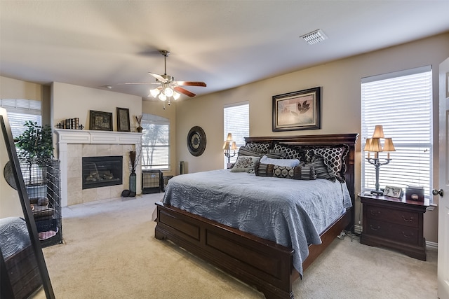 bedroom featuring a fireplace, light carpet, multiple windows, and ceiling fan