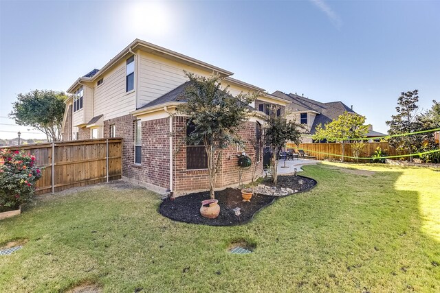view of side of home featuring brick siding, a fenced backyard, and a yard