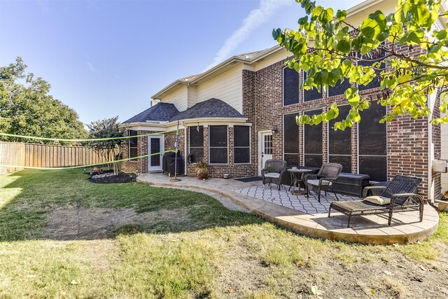 rear view of property with a patio, a shingled roof, fence, a yard, and brick siding