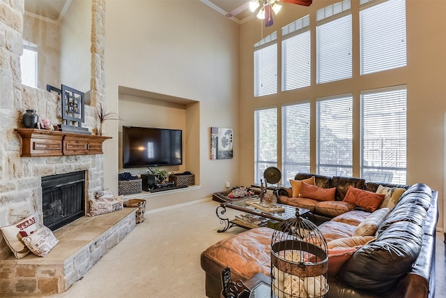 living area with carpet floors, ornamental molding, a ceiling fan, a stone fireplace, and a high ceiling