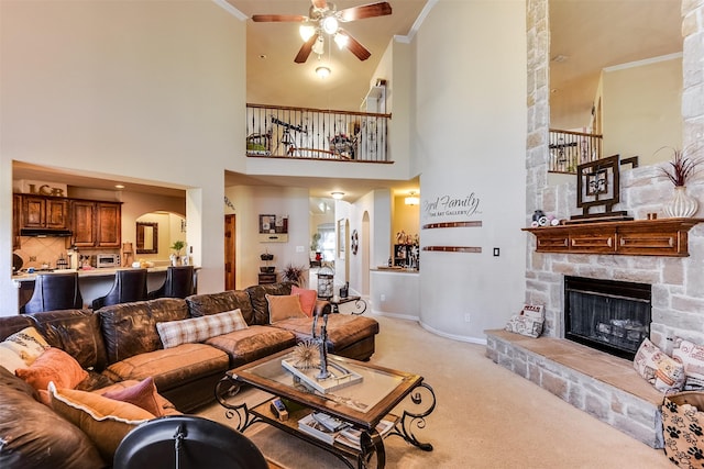 living room with a fireplace, crown molding, a ceiling fan, light carpet, and arched walkways