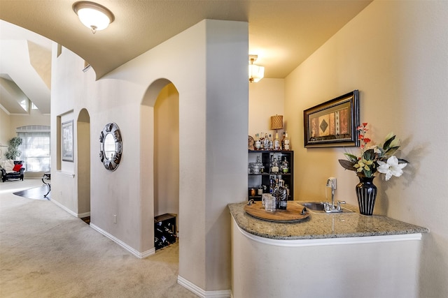 hall with carpet, baseboards, arched walkways, and a sink