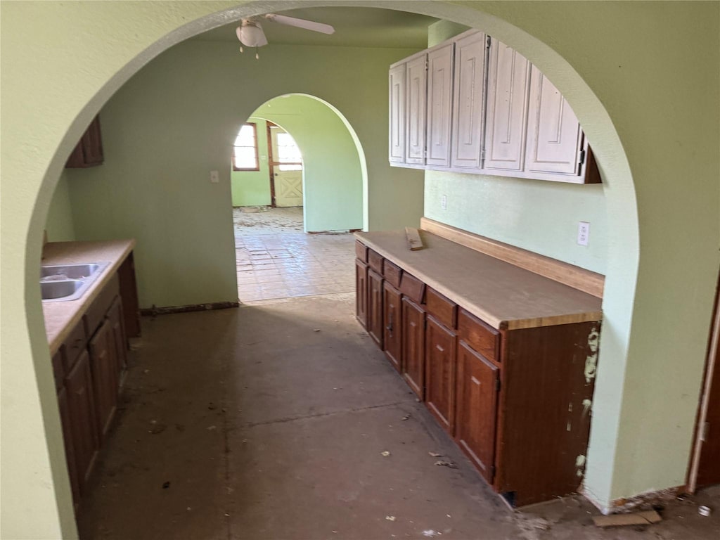 kitchen featuring light countertops, a sink, a ceiling fan, and unfinished concrete floors