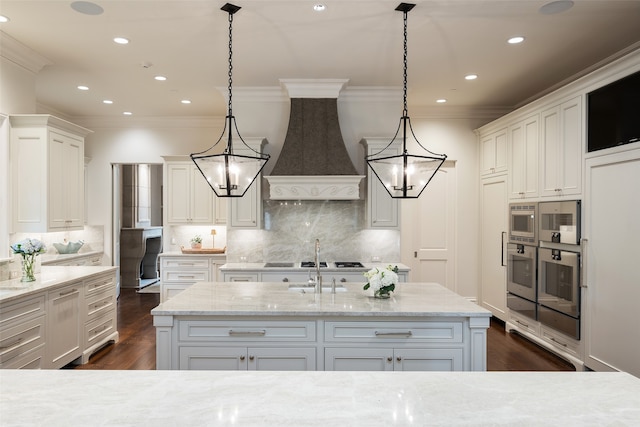 kitchen featuring light stone counters, premium range hood, pendant lighting, and a center island with sink