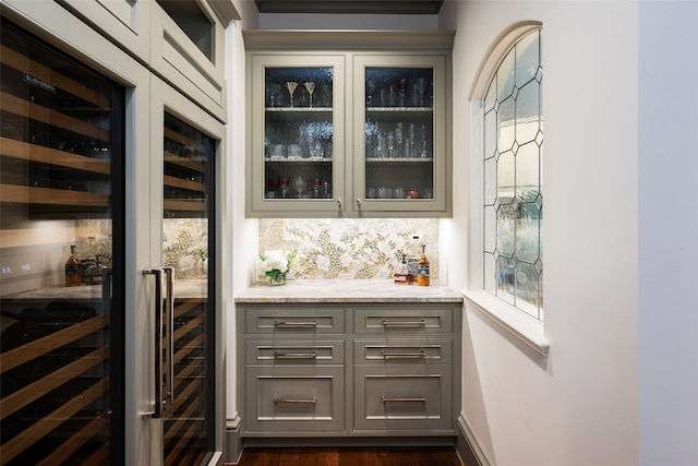 bar with dark hardwood / wood-style flooring, light stone counters, gray cabinetry, and beverage cooler