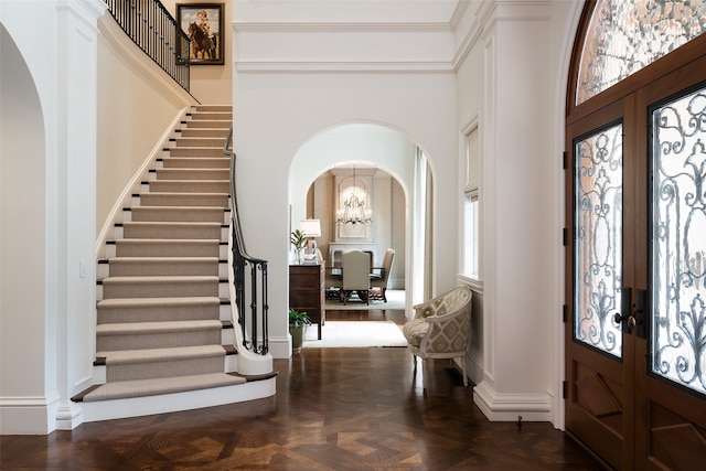 entrance foyer with french doors, a high ceiling, dark parquet floors, ornamental molding, and a chandelier