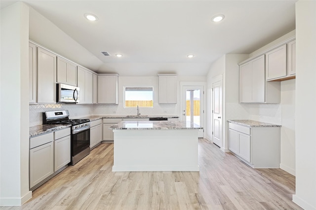 kitchen with sink, light hardwood / wood-style flooring, appliances with stainless steel finishes, light stone countertops, and a kitchen island