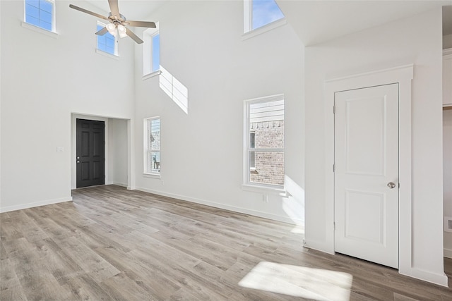 unfurnished living room with ceiling fan, a towering ceiling, and light hardwood / wood-style floors