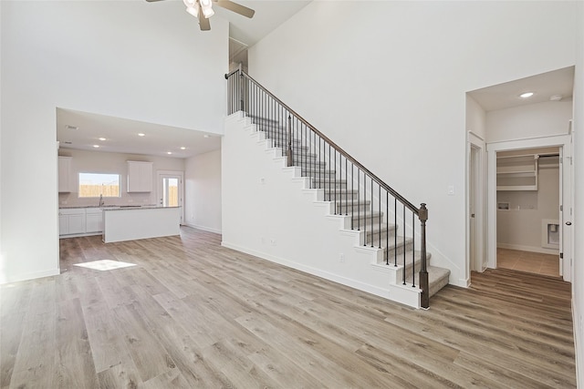 unfurnished living room with ceiling fan, a towering ceiling, sink, and light wood-type flooring