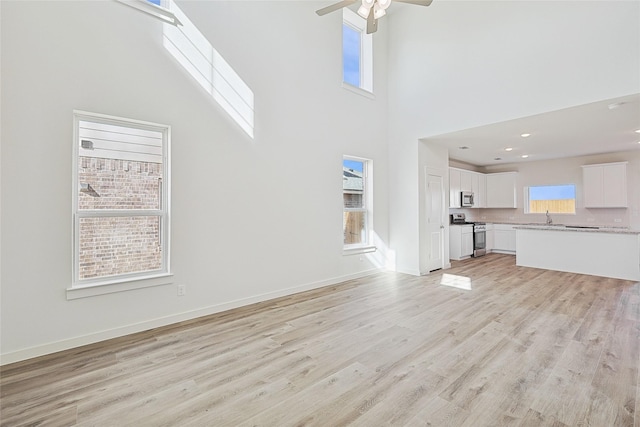 unfurnished living room featuring plenty of natural light, sink, light hardwood / wood-style floors, and a high ceiling