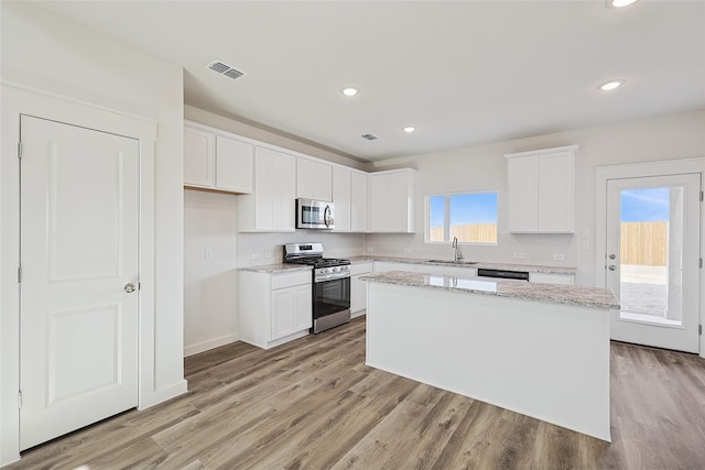 kitchen with sink, a kitchen island, stainless steel appliances, a healthy amount of sunlight, and white cabinets