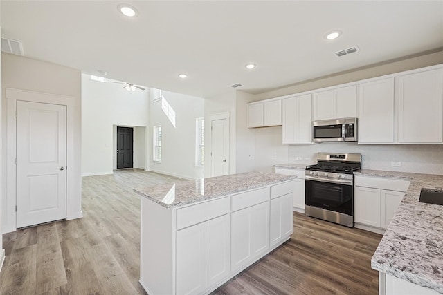 kitchen featuring a kitchen island, appliances with stainless steel finishes, white cabinets, light hardwood / wood-style floors, and light stone countertops