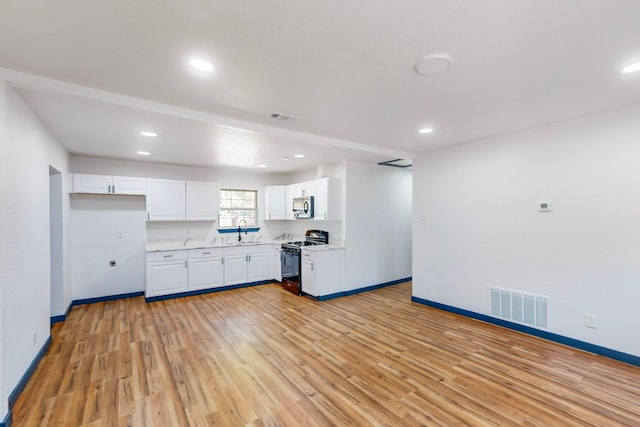 kitchen with light hardwood / wood-style floors, gas range oven, and white cabinets