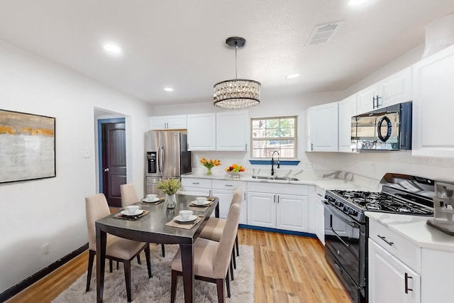 kitchen featuring white cabinets, light hardwood / wood-style flooring, black appliances, pendant lighting, and sink