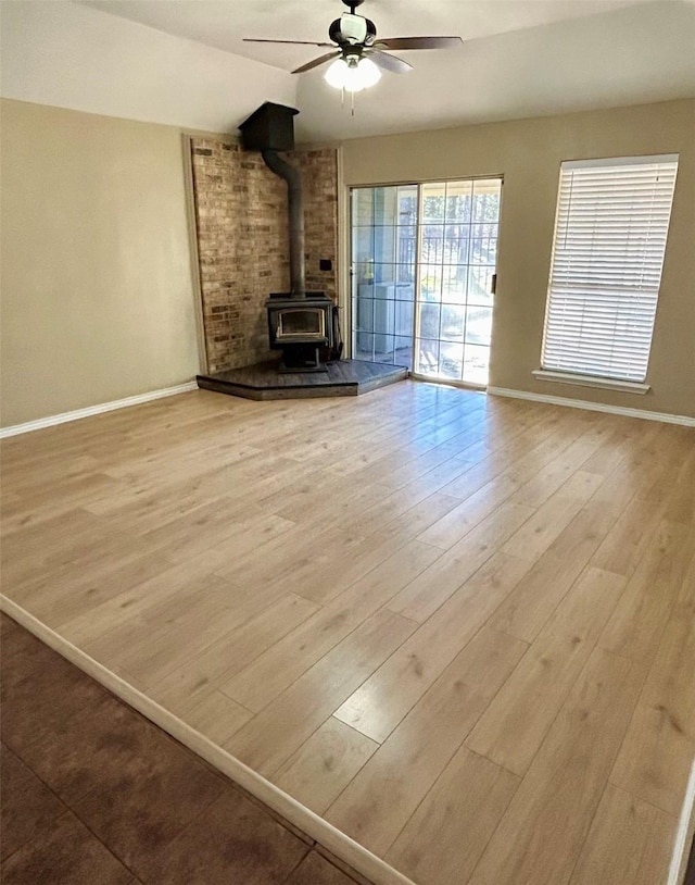 unfurnished living room with light wood-type flooring, a wood stove, ceiling fan, and vaulted ceiling