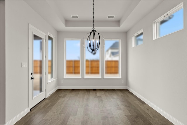 unfurnished dining area featuring an inviting chandelier, visible vents, a raised ceiling, baseboards, and dark wood-style floors