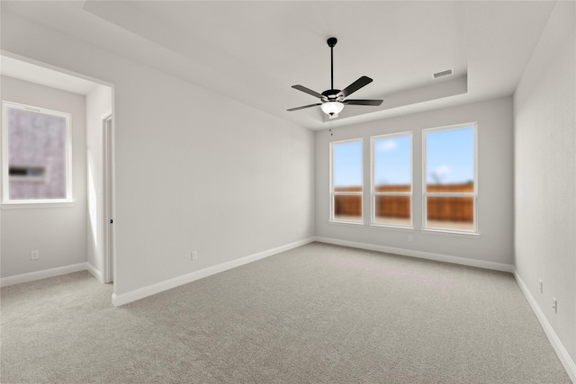 empty room with visible vents, baseboards, a tray ceiling, and light colored carpet
