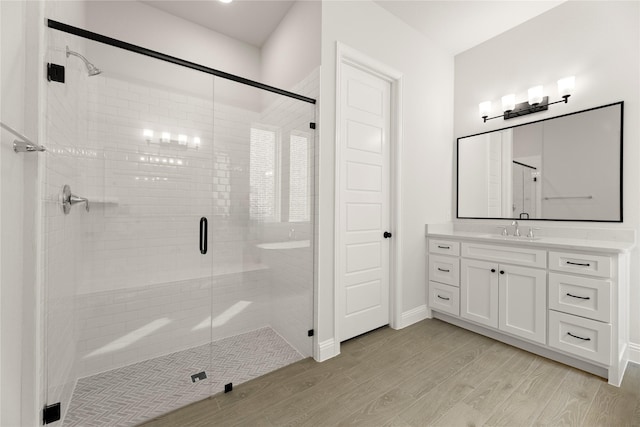 bathroom with a stall shower, wood finished floors, vanity, and baseboards