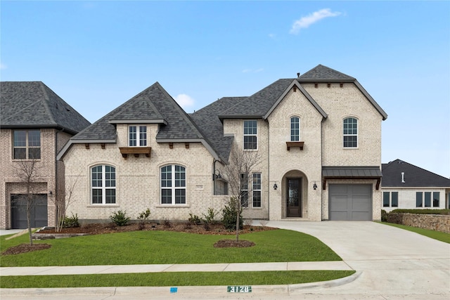 french country style house with roof with shingles, a front lawn, brick siding, an attached garage, and concrete driveway