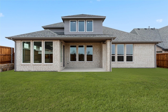 back of house featuring a patio, a lawn, brick siding, fence, and a shingled roof