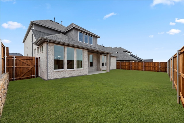 rear view of house featuring brick siding, a shingled roof, a fenced backyard, and a lawn