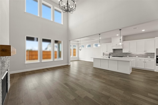 unfurnished living room featuring dark wood-style flooring, a wealth of natural light, an inviting chandelier, and a sink