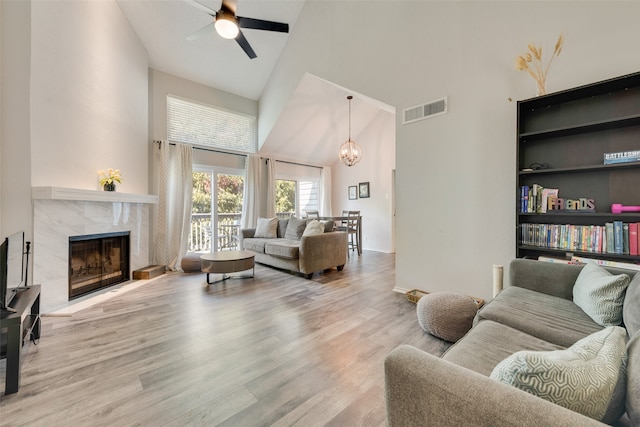 living room with a premium fireplace, built in features, light wood-type flooring, high vaulted ceiling, and ceiling fan with notable chandelier