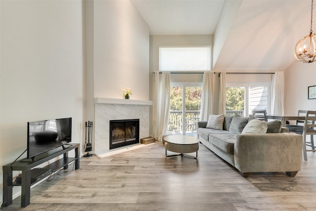 living room with a premium fireplace, lofted ceiling, hardwood / wood-style flooring, and an inviting chandelier