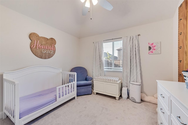 bedroom with a crib, vaulted ceiling, light carpet, and ceiling fan