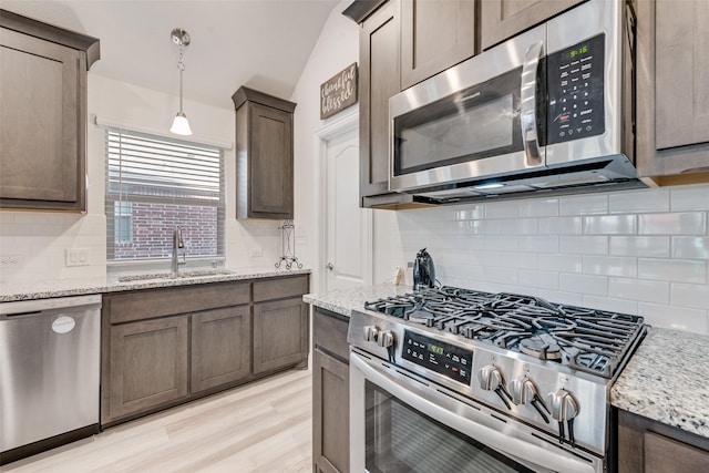 kitchen featuring sink, decorative light fixtures, appliances with stainless steel finishes, light stone countertops, and light hardwood / wood-style floors