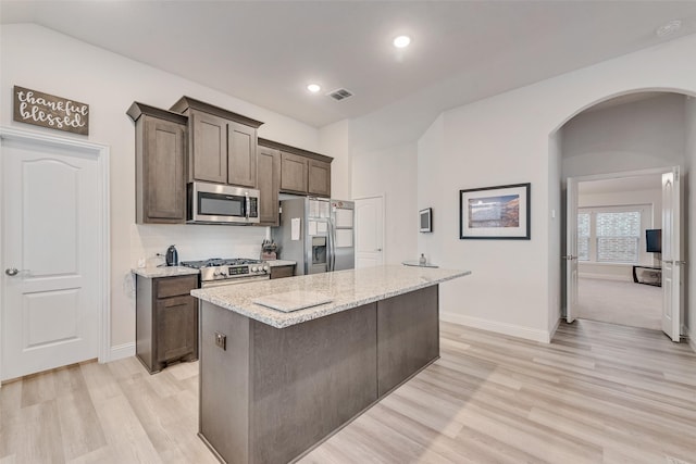 kitchen with appliances with stainless steel finishes, a center island, light stone counters, and light wood-type flooring