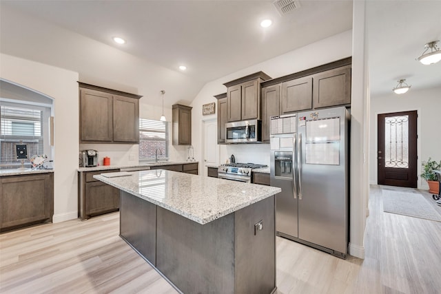 kitchen with pendant lighting, stainless steel appliances, a center island, light stone countertops, and light hardwood / wood-style floors