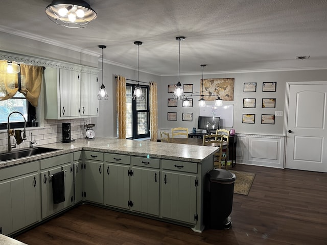 kitchen with sink, kitchen peninsula, hanging light fixtures, ornamental molding, and dark hardwood / wood-style floors