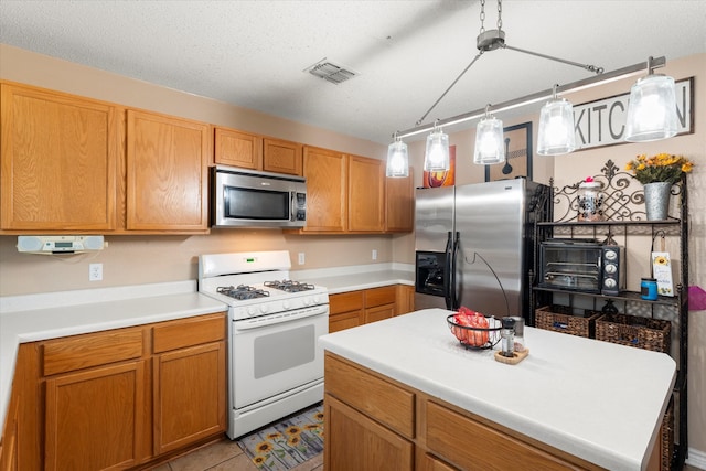 kitchen with hanging light fixtures, light tile patterned flooring, a textured ceiling, a kitchen island, and appliances with stainless steel finishes