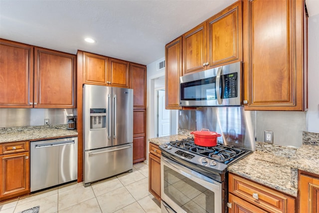 kitchen featuring light tile patterned floors, appliances with stainless steel finishes, and light stone counters