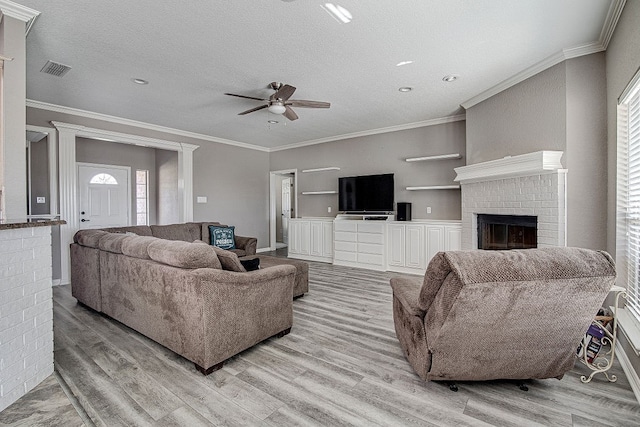 living room with light hardwood / wood-style floors, crown molding, a fireplace, and ceiling fan