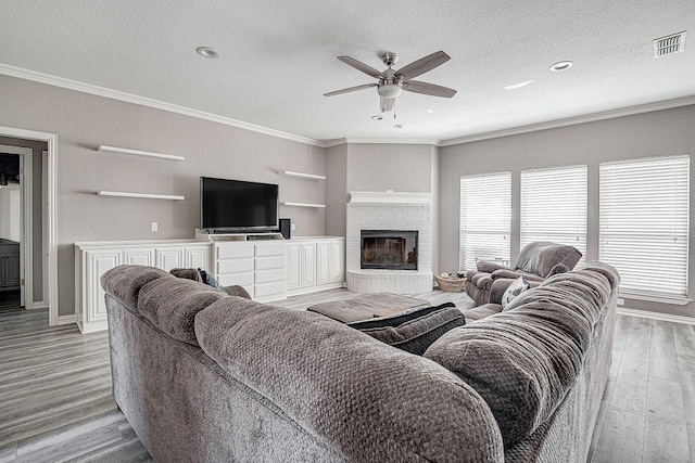 living room featuring ornamental molding, a brick fireplace, light wood-type flooring, a textured ceiling, and ceiling fan