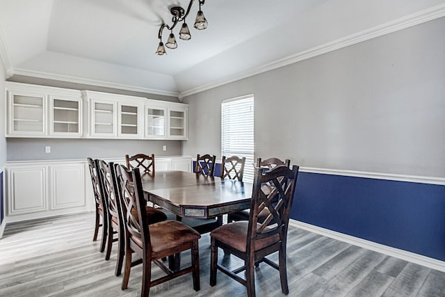 dining area with light hardwood / wood-style floors, crown molding, lofted ceiling, and a raised ceiling