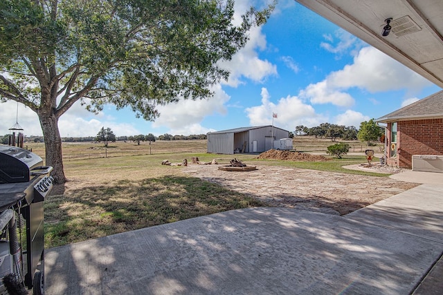 view of yard with a patio area, a fire pit, a storage unit, and a rural view