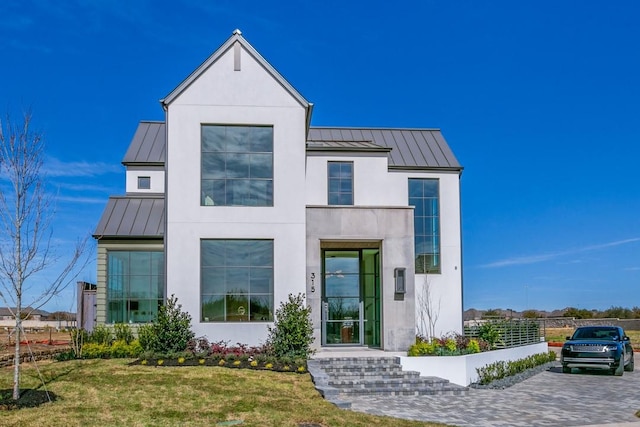 view of front of home with metal roof, a front yard, stucco siding, and a standing seam roof