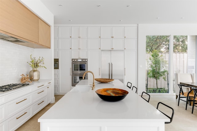 kitchen featuring a center island with sink, appliances with stainless steel finishes, backsplash, and white cabinets