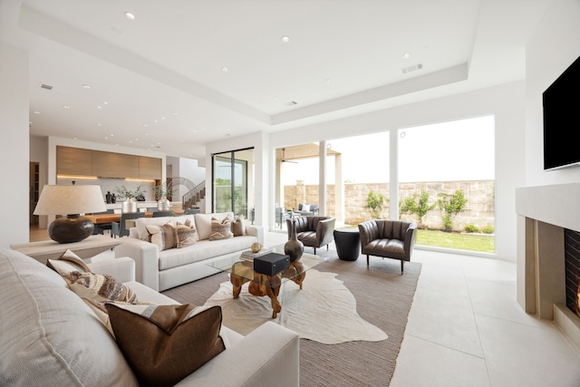 living area with a tray ceiling, recessed lighting, a premium fireplace, stairway, and light tile patterned floors